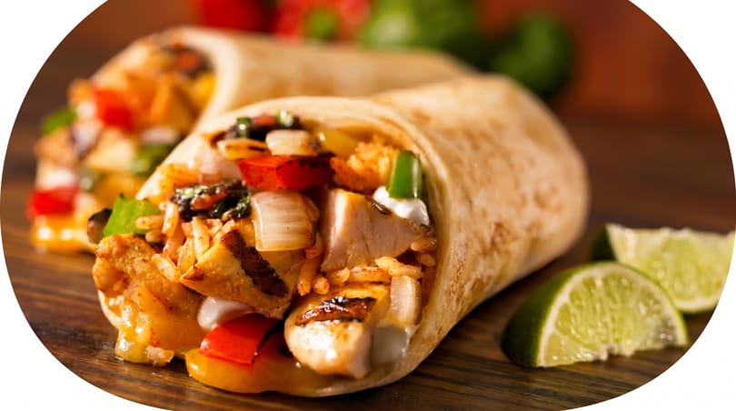 Two chicken burritos filled with rice, peppers, and onions, served with lime wedges on a wooden surface.