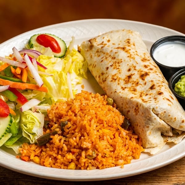 A burrito, Spanish rice, and a side salad with guacamole and sour cream on a white plate.