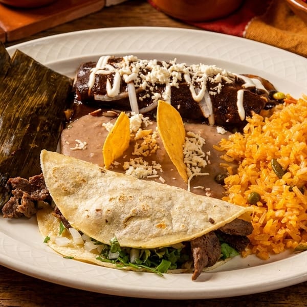 A white plate with a tamale, enchilada, refried beans, rice, and a steak taco on a wooden table.