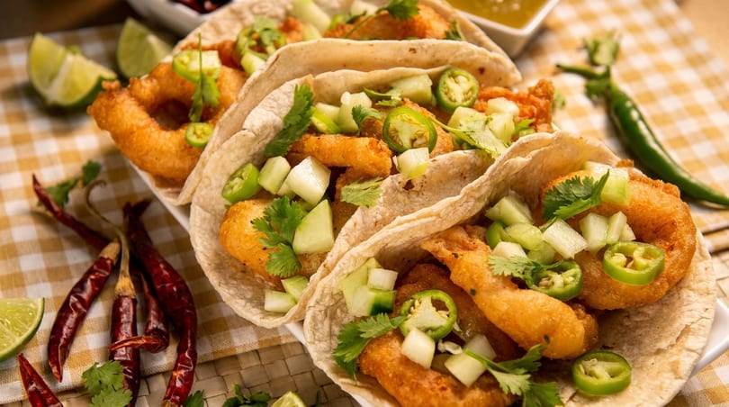 Three shrimp tacos with cucumber, jalapeños, and cilantro, on a checkered tablecloth.